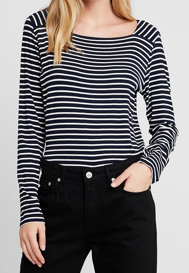 Camicia a maniche lunghe a righe in blu navy e bianco, con una scollatura ampia e una silhouette aderente. Abbinata a jeans neri a vita alta.