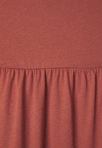 Un tissu de couleur rouille, doux, avec une texture côtelée sur le dessus et une partie froncée en bas. Un design simple sans motifs supplémentaires.