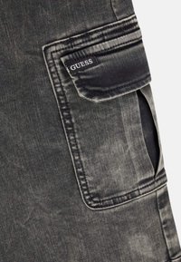 Tissu en denim noir avec une poche à rabat dotée d'une petite étiquette noire avec le texte blanc "GUESS".