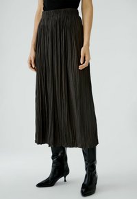 Zwarte geplooide midi-rok met een elastische tailleband; zachte, vloeiende stof; gecombineerd met zwarte puntige enkelboots.