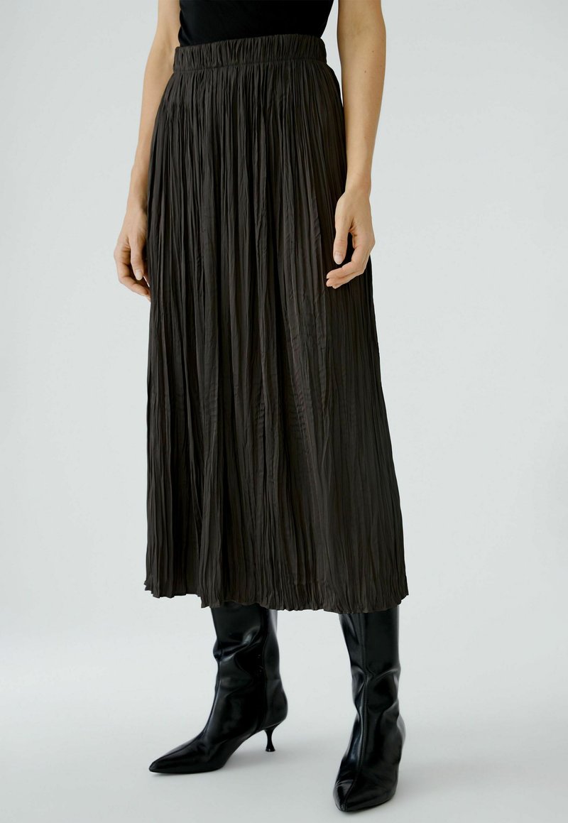 Black pleated midi skirt with an elastic waistband; soft, flowing fabric; paired with black pointed ankle boots.