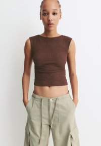 Top cropped de culoare maronie, ajustat, dintr-un material texturat. Asortat cu pantaloni cargo lejeri, de culoare verde deschis, cu buzunare laterale și talie cu șnur.