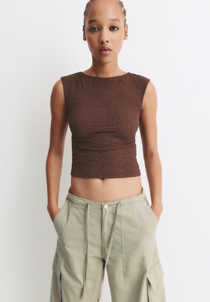 Crop top marron ajusté en tissu texturé. Associé à un pantalon cargo léger vert clair avec des poches latérales et une taille à cordon de serrage.
