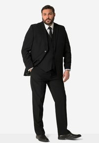 Completo nero a tre pezzi composto da giacca attillata, gilet e pantaloni, realizzato in tessuto liscio, con camicia bianca e cravatta nera. Scarpe nere completano l'outfit.