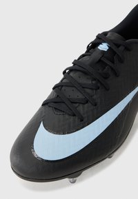 Crampons de football noirs avec une surface texturée, dotées d'un swoosh Nike bleu clair et de lacets noirs. Studs visibles sur la semelle pour une meilleure traction.