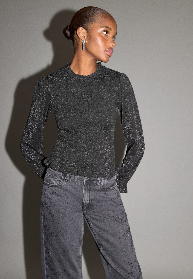 Top nero a maniche lunghe a coste con orlo arricciato, abbinato a jeans grigi con decorazioni scintillanti. Tessuto liscio, design aderente.