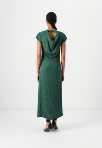 Green, long dress with a draped back, short sleeves, and a keyhole detail. Smooth texture, subtle pattern, paired with strappy black heels.