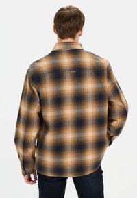 Skjorte med tern i nuancer af brun, blå og grå. Har krave med knapper og rygpanel. Materialet ser tekstureret ud med en blød overflade.