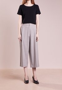 Black cotton t-shirt paired with high-waisted, light gray wide-leg trousers, featuring a smooth texture and sharp pleats, complemented by black heels.