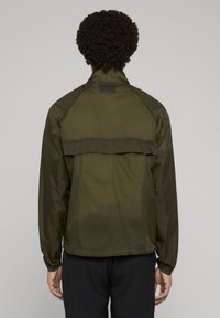 Lekka kurtka oliwkowa z suwakiem przy kołnierzu, długimi rękawami i detalem w postaci tylnej klapki. Gładka faktura, praktyczny design, podstawowe dopasowanie.