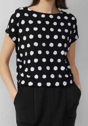 Czarny t-shirt z krótkim rękawem w białe kropki o różnych rozmiarach, z okrągłym dekoltem i luźnym fasonem.