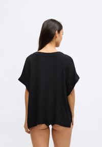 Črn, sproščen zgornji del z kratkimi rokavi, okroglim izrezom, vodoravnimi šivi in stranskimi zarezi. Tekstura deluje mehka in padajoča.