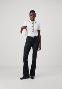 Polo à manches courtes côtelé blanc avec des finitions noires et des détails de boutons, associé à un jean flare en denim foncé et des chaussures noires à bout pointu.