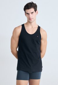 Svart tanktop laget av bomull, med rund hals og uten ermer. Inkluderer en liten logo på venstre brystområde.