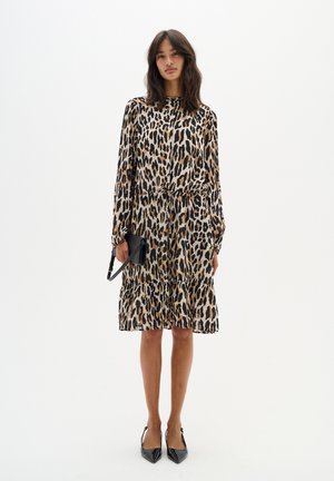Kjol med leopardmönster, långa ärmar, elastisk midja och lager på lager-skick. Tillverkad av lätt material, tillsammans med en svart kuvertväska och klackar.