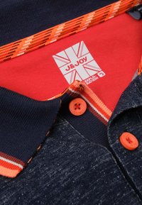 Donkerblauwe polo met oranje knopen en gestreepte kraag. Etiket heeft een ontwerp van de Britse vlag. De stof heeft een textuur en een gemengde uitstraling.