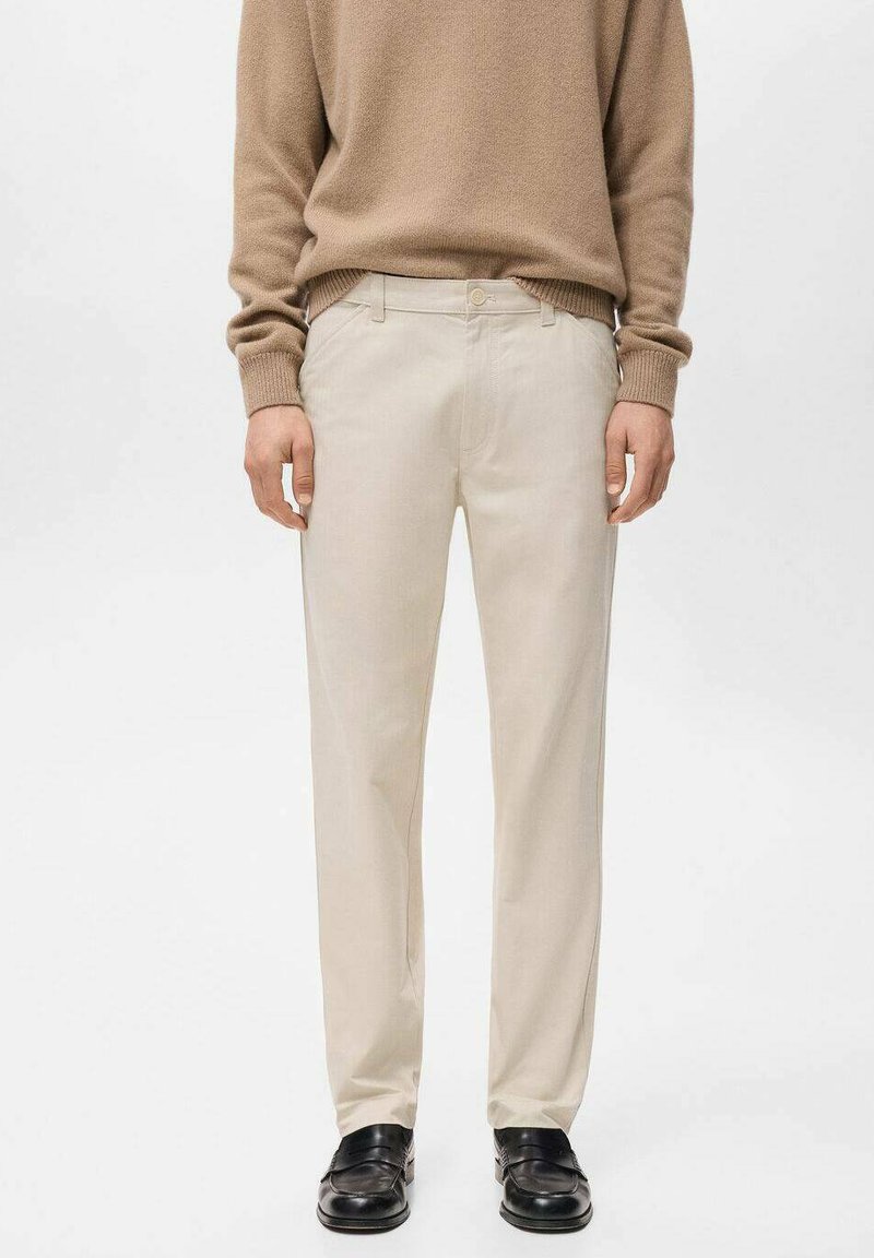 Pantalones beige de corte recto, fabricados con tejido de trama, con cremallera y trabillas para cinturón, combinados con zapatos negros.