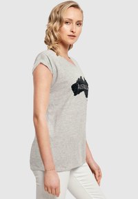 Graues Baumwoll-T-Shirt mit V-Ausschnitt und umgekrempelten kurzen Ärmeln. Mit einem schwarzen Australien-Karten-Graphic und einem entspannten Schnitt.