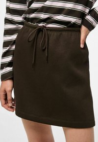 Gonna marrone scuro realizzata in tessuto morbido con vita elastica e cordino, caratterizzata da un design semplice e minimalista.