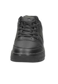 Zapatilla de piel negra con detalles perforados, puntera redondeada y cordones planos. Con una suela de goma texturizada y un sutil logo en la lengüeta.