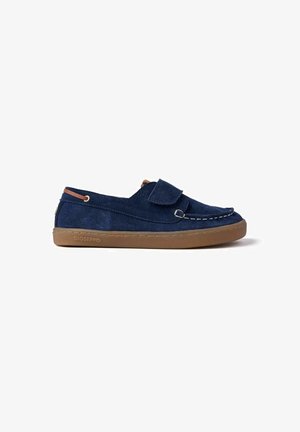 Scarpe slip-on in camoscio blu navy con suola in gomma marrone, caratterizzate da un dettaglio cucito e una chiusura a strappo. Design minimalista per una calzata facile.