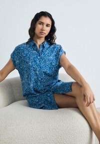 Kortermet skjorte med knapper og matchende shorts, blå med hvitt blomster mønster, avslappet passform, glatt tekstur og sidespalter.