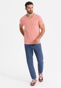 Světle růžové tričko s výstřihem do V v slim fit, spárované s modrými džínami a červenými teniskami. Tento outfit se vyznačuje ležérním, moderním designem.