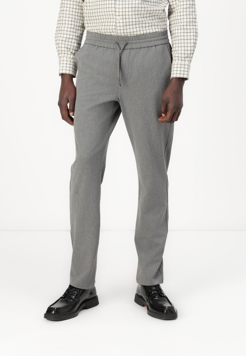 Pantaloni grigi con vita elasticizzata, taglio affusolato e tasche laterali, abbinati a scarpe nere con lacci, caratterizzate da un tessuto testurizzato.