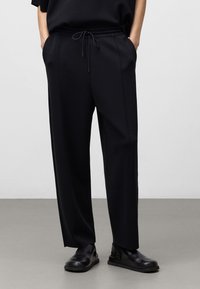 Zwarte, relaxed-fit broek met elastische tailleband en koord. Bevat zijzakken en een zachte, licht gestructureerde stof.