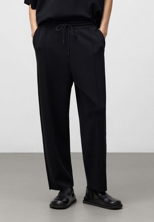 Black, relaxed-fit pants with elastic waistband and drawstring. Features side pockets and a smooth, slightly textured fabric.