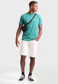 Sinine puuvillane t-särk, valged lühikesed püksid ja mustad spordijalatsid. Rinnal on väike logo ning kaasa tuleb must risti kantav kott.