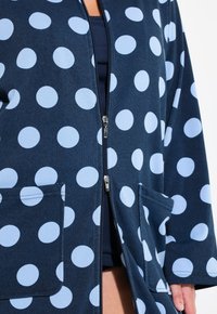 Cardigan zip con zip navy con grandi pois blu chiaro, dotato di due tasche frontali e con una texture di tessuto morbido e liscio.