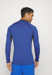 Langarm sportshirt van textuurstof in blauwe kleur met zwarte accenten onder de armen en op de kraag; nauwsluitend ontwerp met een ronde halslijn.