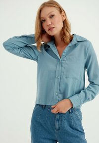 Lichtblauw, langarm knoopshirt met een kraag en zak, gecombineerd met hoge taille denim jeans. Gladde textuur, relaxte pasvorm.