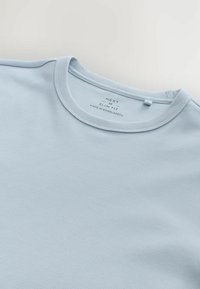 Světle modré slim-fit tričko vyrobené z žebrované tkaniny. Má kulatý výstřih s prošitým lemem a štítek označující původ a značku.