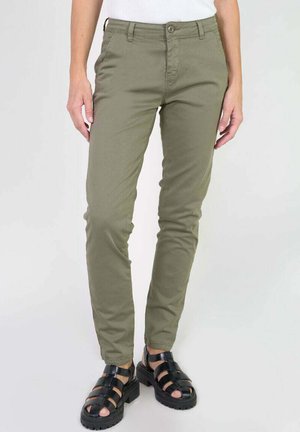 Slim-fit olive green pants worn with black chunky open-toe sandals on a person standing against a plain background.