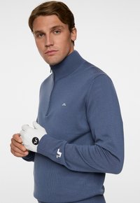 Meriine sinine kapuutsiga sviiter, millel on soonikkrae, valmistatud pehmest kangast. Valged nahkkindad, millel on logo, täiustavad riietust. Minimalistlik disain.