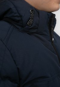 Navy Kapuzenjacke mit strukturiertem Design, strukturiertem Stoff, sichtbarem Reißverschluss und dekorativem schwarzen Kordelzug am Kragen.