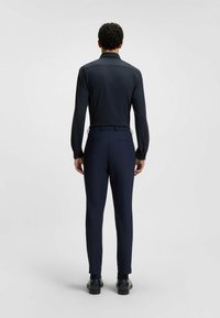 Camicia a maniche lunghe blu navy con una texture liscia, abbinata a pantaloni eleganti. Entrambi i capi hanno una vestibilità slim e un design minimalista.