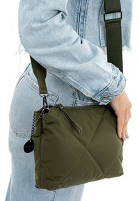 Quilted olive green handbag with a zipper, chain accent, and adjustable strap, showcased against a light denim outfit.