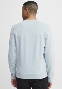 Világoskék pulóver hosszú ujjakkal, bordázott mandzsettával és szegéllyel, kerek nyakkal és sima textúrával. Egyszerű design, minta nélkül.