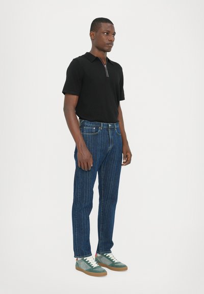 Cămașă polo neagră, blugi din denim cu dungi albastre, adidași verzi și gri cu șireturi albe. Design simplu, croială dreaptă.