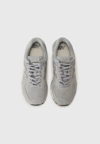 Pelēki sporta apavi ar teksturētu zamša augšdaļu, sieta akcentiem, apaļām auklām un gumijas zoli. Uzvalkā New Balance logotipu uz mēles.