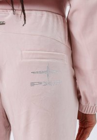 Roze velours broek met een achterzak en een zilveren rhinestone logo-accent. Gladde textuur met een elastische tailleband en gathered mouwen.