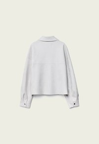 Veste blanche courte en tissu lisse. Présente un col, des manches longues avec des accents de boutons, et un design épuré et minimaliste.
