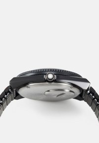 Black watch with a metal bracelet, round case, textured bezel, and a screw-down crown. Features a smooth silver back and minimalist design.