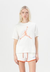 White t-shirt with an orange Jordan logo in the center. The shirt has a loose fit and is paired with white shorts featuring orange accents.