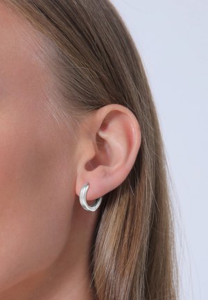 Silberner Ohrstecker mit einer glatten, polierten Oberfläche. Kreisform, mittlere Größe, auf dem Ohrläppchen dargestellt, gegen glattes Haar.