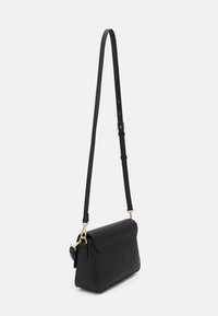 Svart texturerad läder crossbody-väska med lång justerbar rem och detaljer i guldton på vit bakgrund.