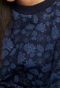 Sudadera azul marino con un patrón floral en azul claro, que presenta un cuello redondo acanalado y un delicado logo bordado.